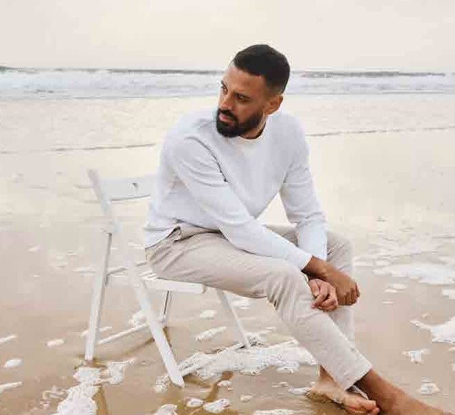 Model in a linen shirt and light trousers seated on the beach